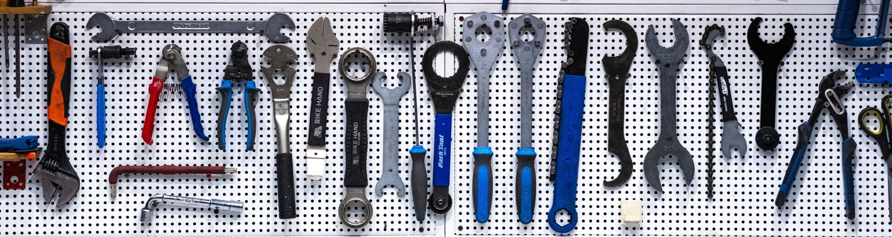 An der Wand sind verschiedene Handwerkzeuge, darunter Schraubenschlüssel, Zangen und Schraubenzieher, ordentlich aufgereiht. Auf der Werkbank darunter liegen ein Maßband und eine Fahrradpumpe. Sparkpoint Executive Coaching.
